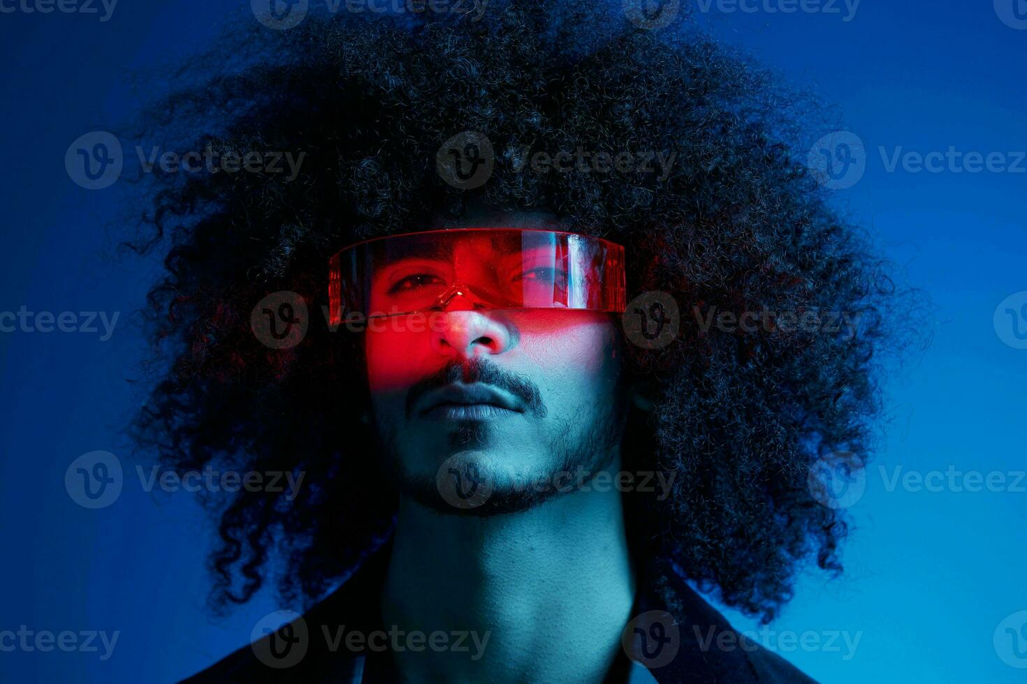moda retrato do uma homem com encaracolado cabelo em uma azul fundo vestindo vermelho oculos de sol, multinacional, colori luz, na moda, moderno conceito. foto
