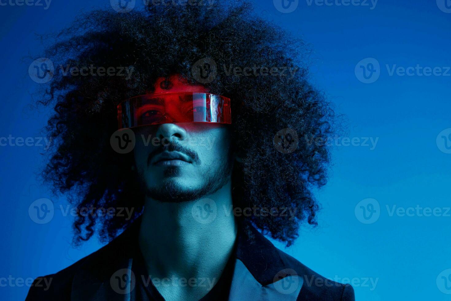 moda retrato do uma homem com encaracolado cabelo em uma azul fundo vestindo vermelho oculos de sol, multinacional, colori luz, na moda, moderno conceito. foto