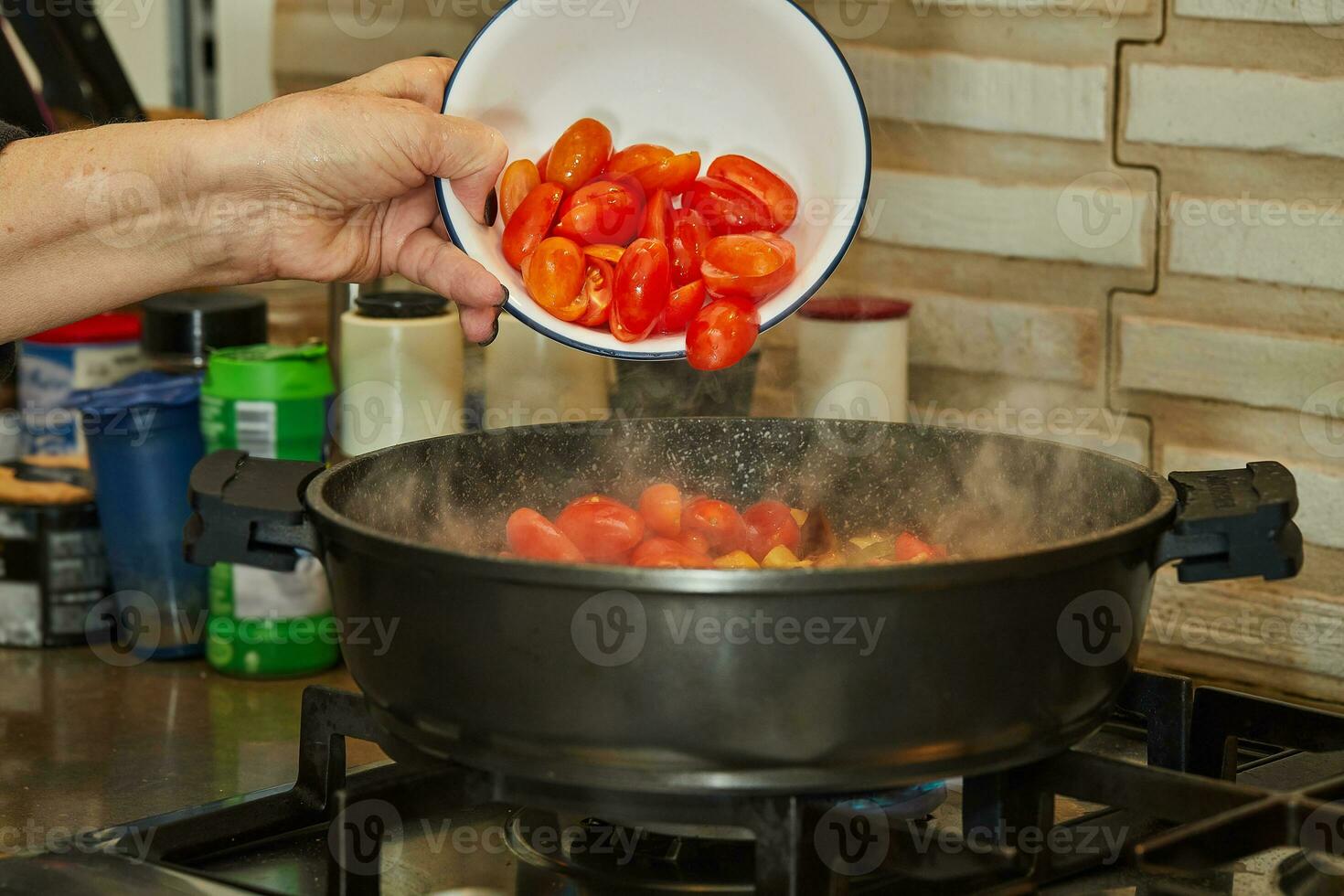 chefe de cozinha lança tomates para dentro uma fritar panela em uma gás fogão foto