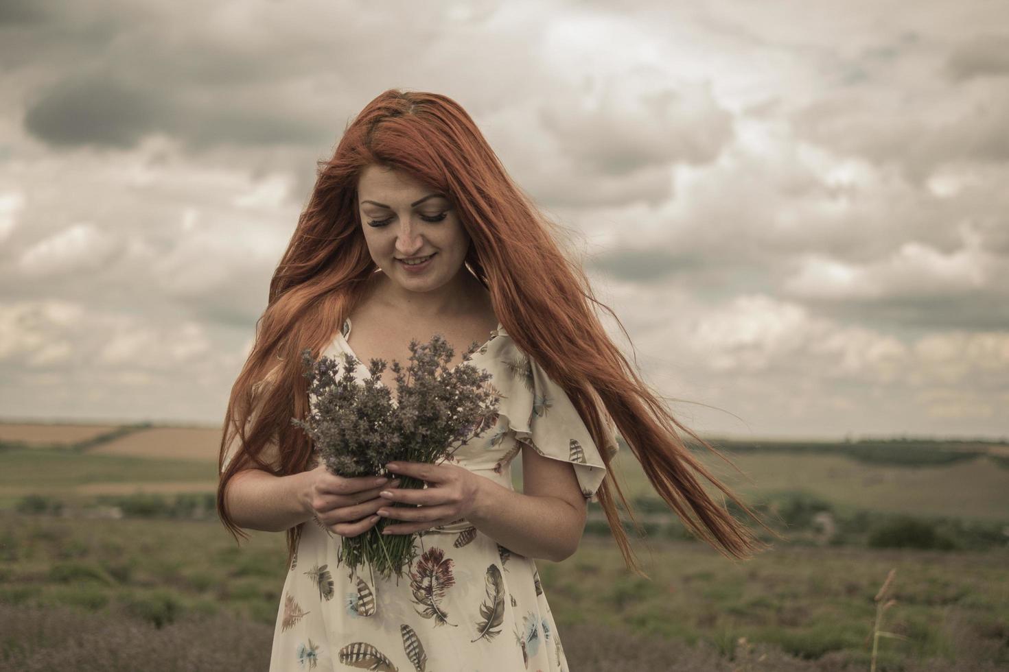 retrato de uma jovem ruiva em um vestido branco em um campo com um buquê de lavanda foto