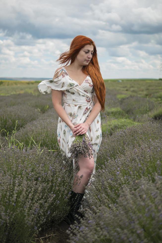 retrato de uma jovem ruiva em um vestido branco em um campo com um buquê de lavanda foto