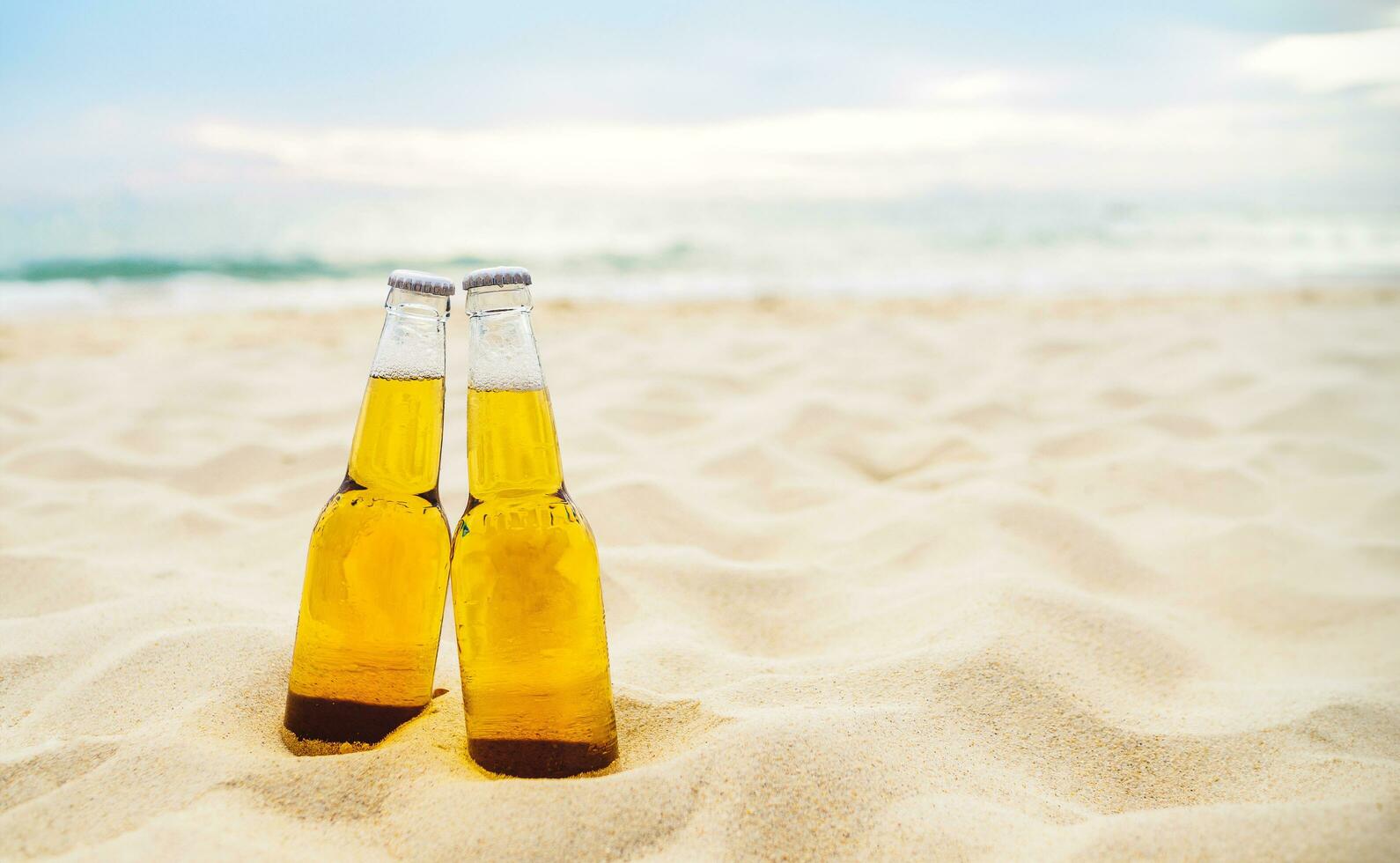 garrafas do Cerveja em a arenoso de praia com mar oceano fundo. festa, amizade, Cerveja conceito. foto