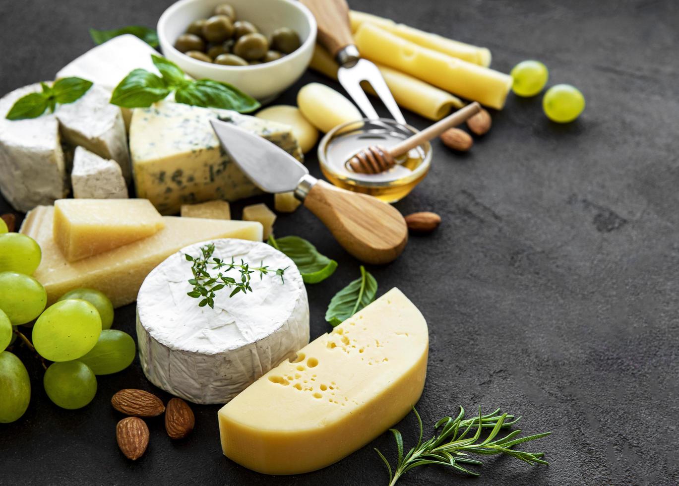 vários tipos de queijo, uvas, mel e salgadinhos em um fundo de concreto preto foto