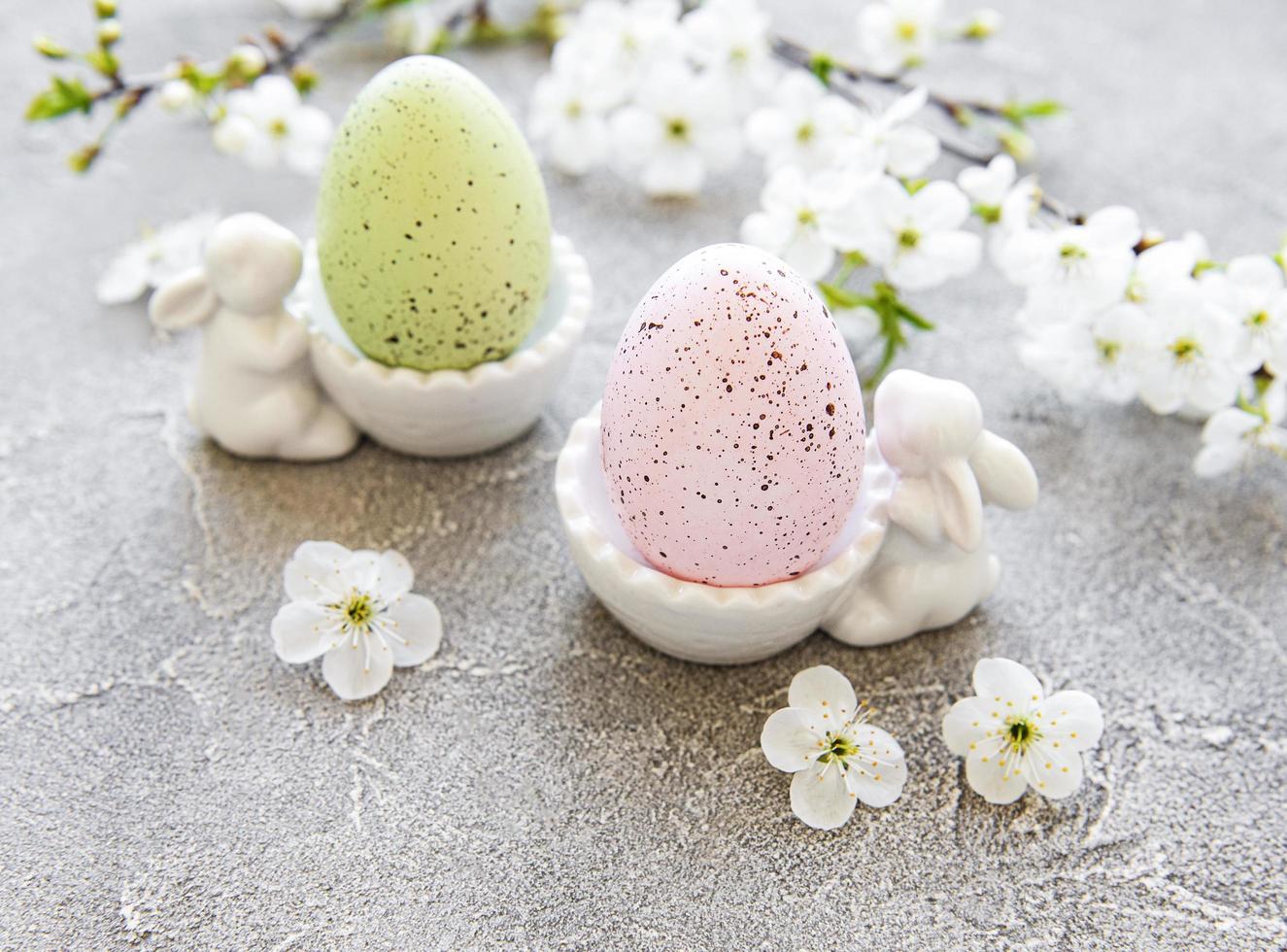 Ovos de Páscoa coloridos em um suporte com estatuetas de coelhinho da Páscoa de cerâmica e flores de primavera em um fundo cinza de concreto foto