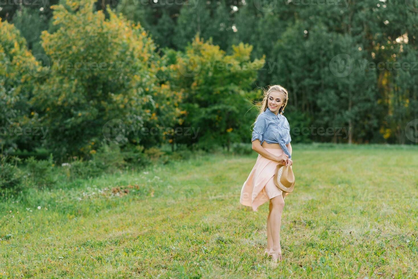 feliz caucasiano jovem mulher, menina caminhando dentro a verão ao ar livre dentro natureza, segurando uma chapéu dentro dela mãos foto