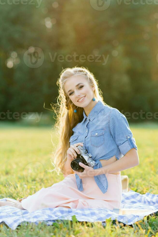 uma lindo jovem mulher detém uma retro Câmera dentro dela mãos. verão piquenique foto