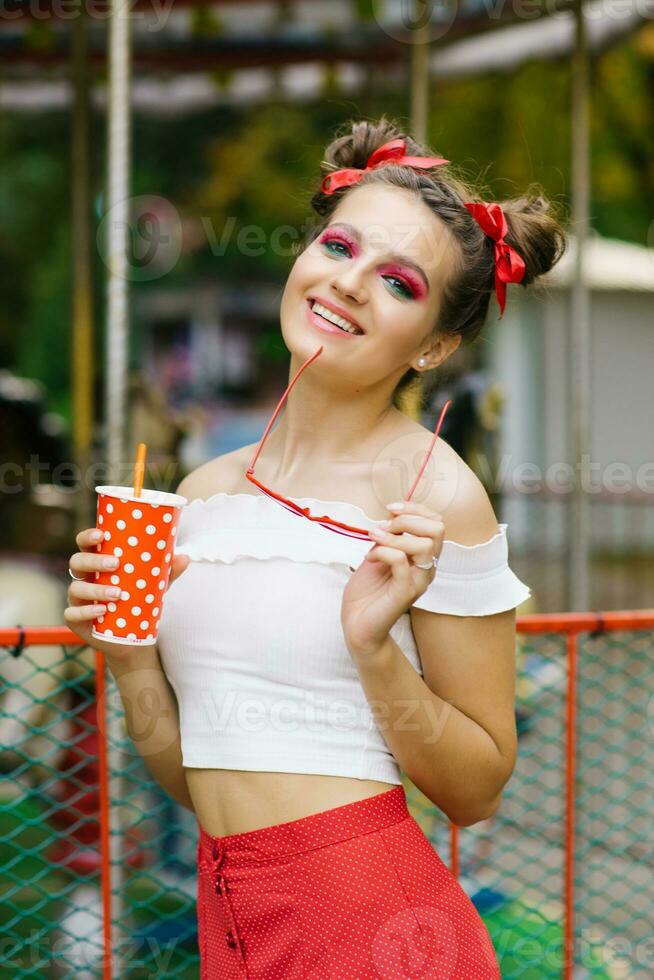 uma bonita menina detém uma papel eco vidro dentro dela mãos e anda em dentro a verão ao ar livre dentro a diversão parque foto