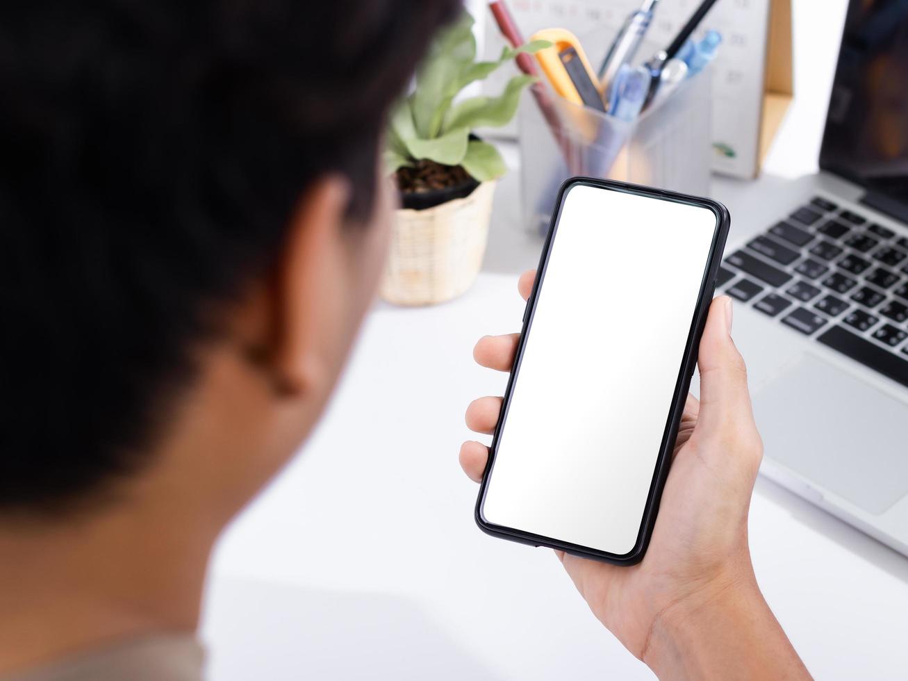 homem usando uma simulação de tela em branco de smartphone na mesa de escritório branca foto