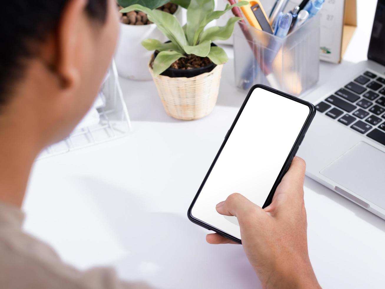 homem usando uma simulação de tela em branco de smartphone na mesa de escritório branca foto