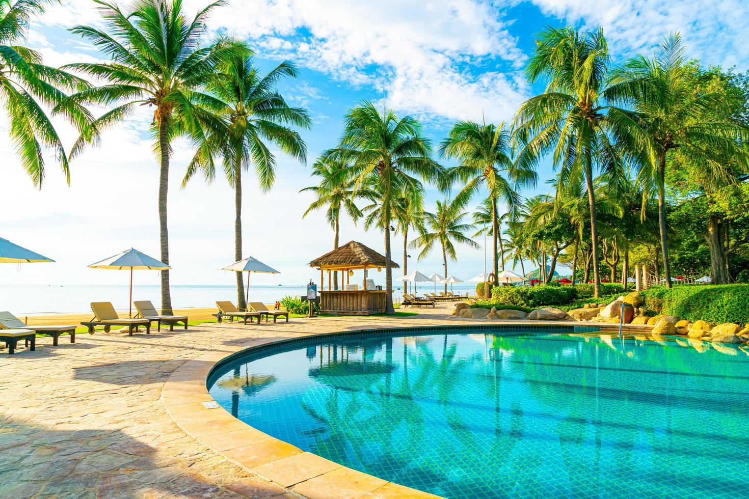 lindo guarda-sol de luxo e cadeira ao redor da piscina externa em hotel e resort com coqueiro no céu azul foto