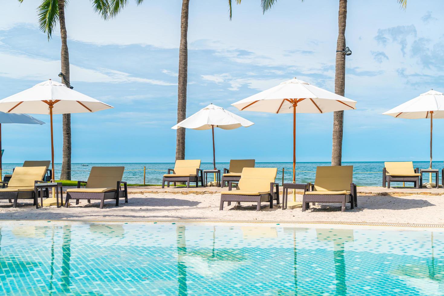 bela praia tropical e mar com guarda-sol e cadeira ao redor da piscina em hotel resort foto