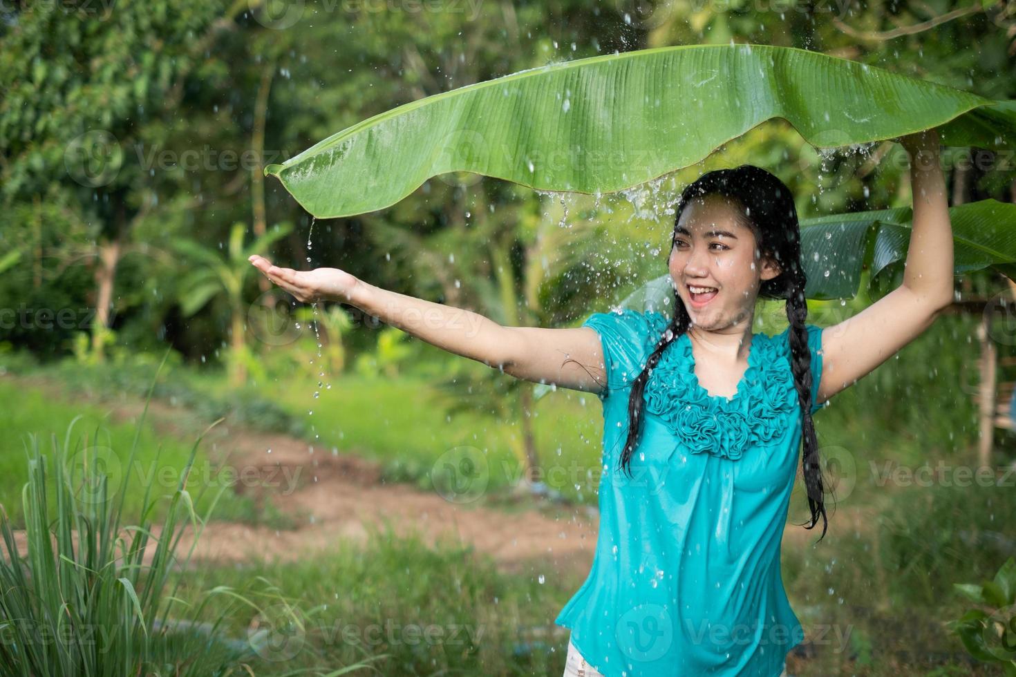 imagem borrada retrato de uma jovem asiática com cabelo preto segurando uma folha de bananeira na chuva no fundo do jardim verde foto