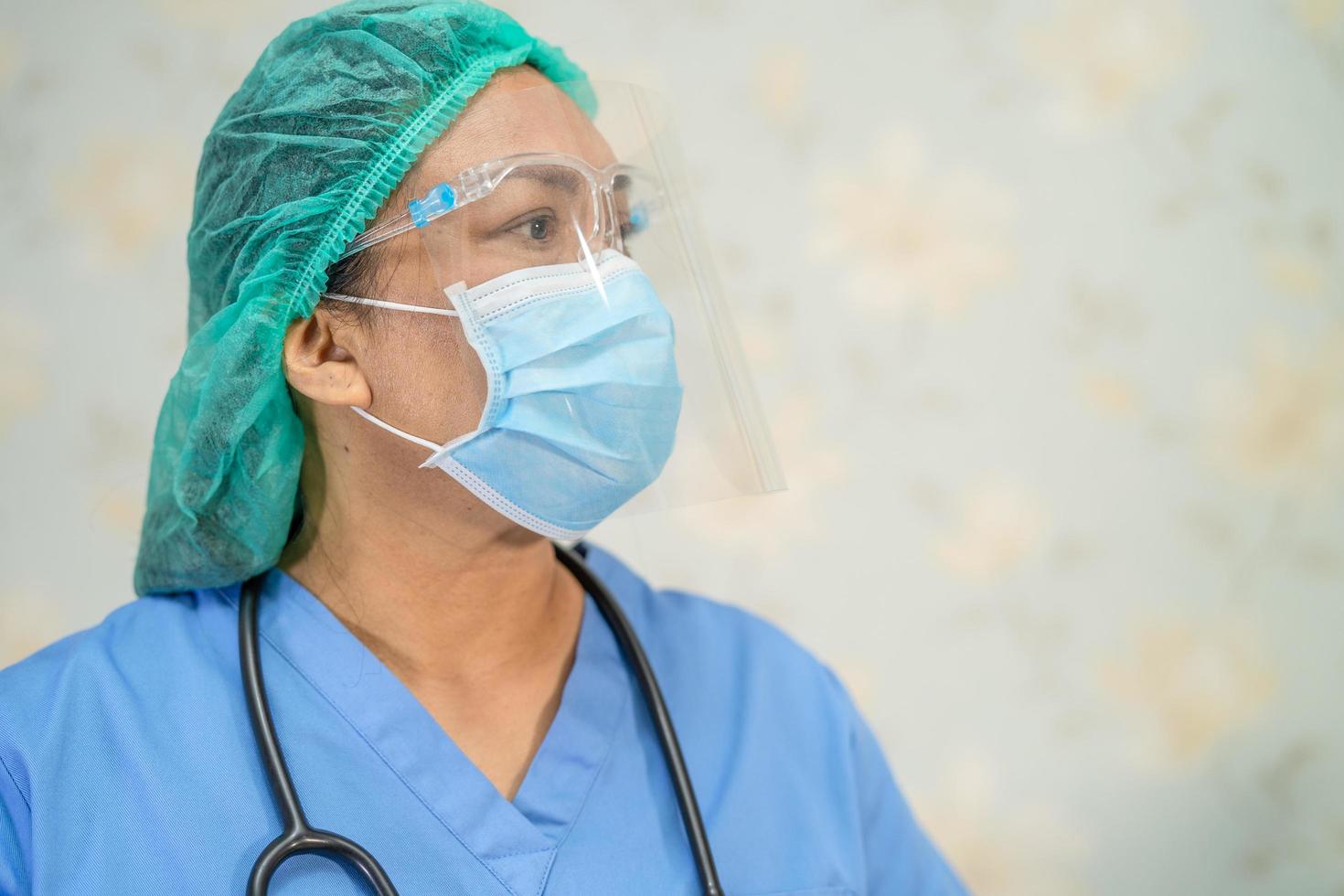 médico asiático usando protetor facial e terno novo normal para verificar paciente proteger segurança infecção covid 19 surto de coronavírus na enfermaria de quarentena do hospital foto