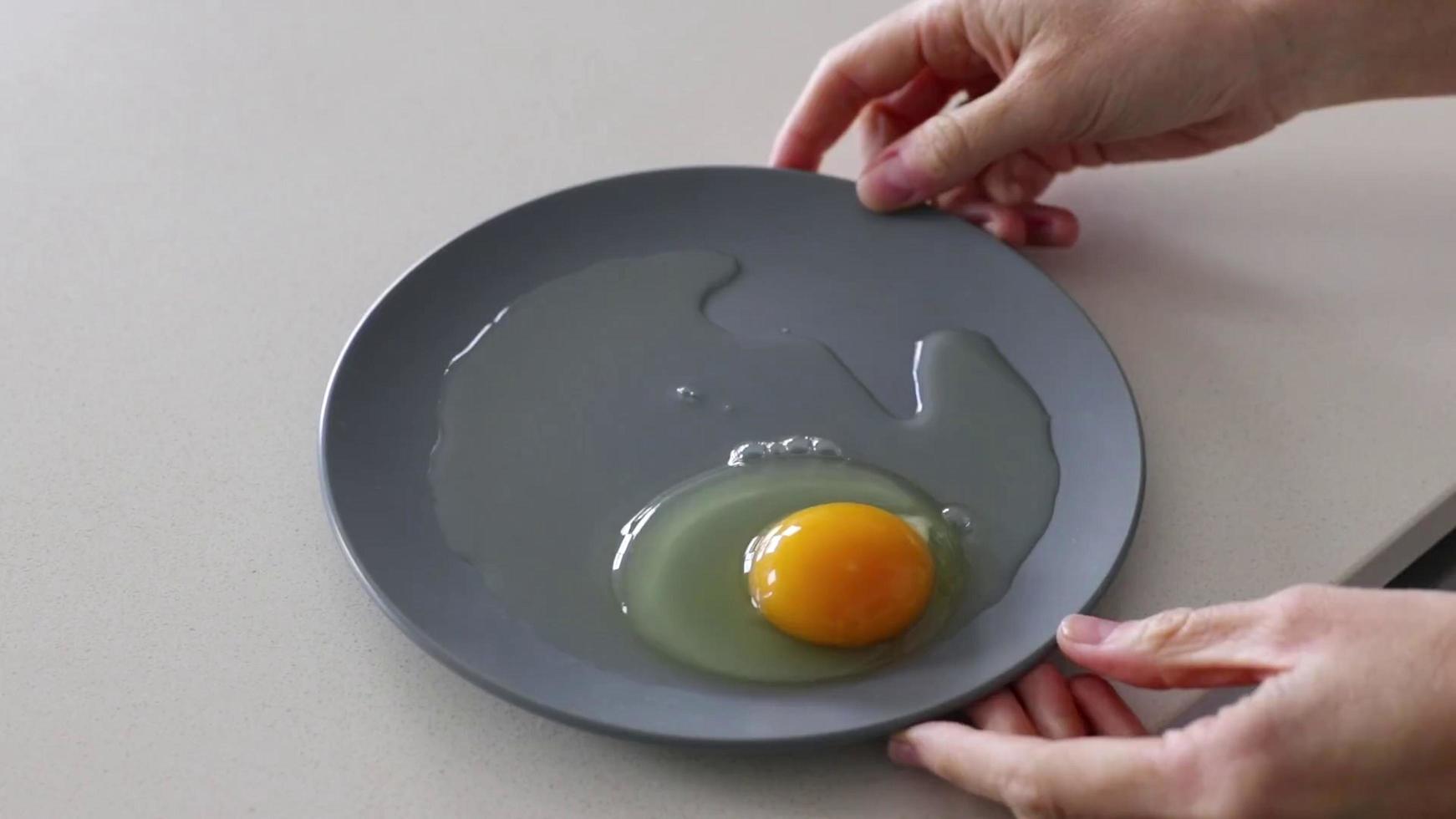 mão segurando um prato cinza com uma gema de ovo dentro foto