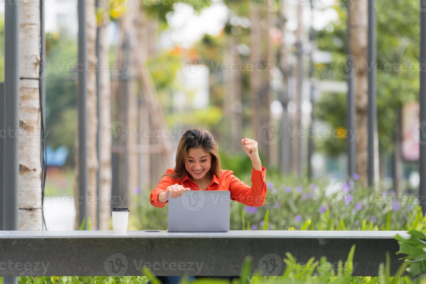 Mulher jovem e bonita com rosto feliz e surpreso usando laptop em um parque da cidade foto