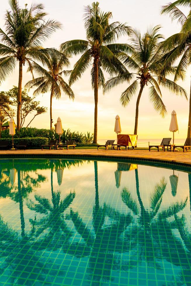 guarda-chuva e cadeira ao redor da piscina em hotel resort com nascer do sol pela manhã foto