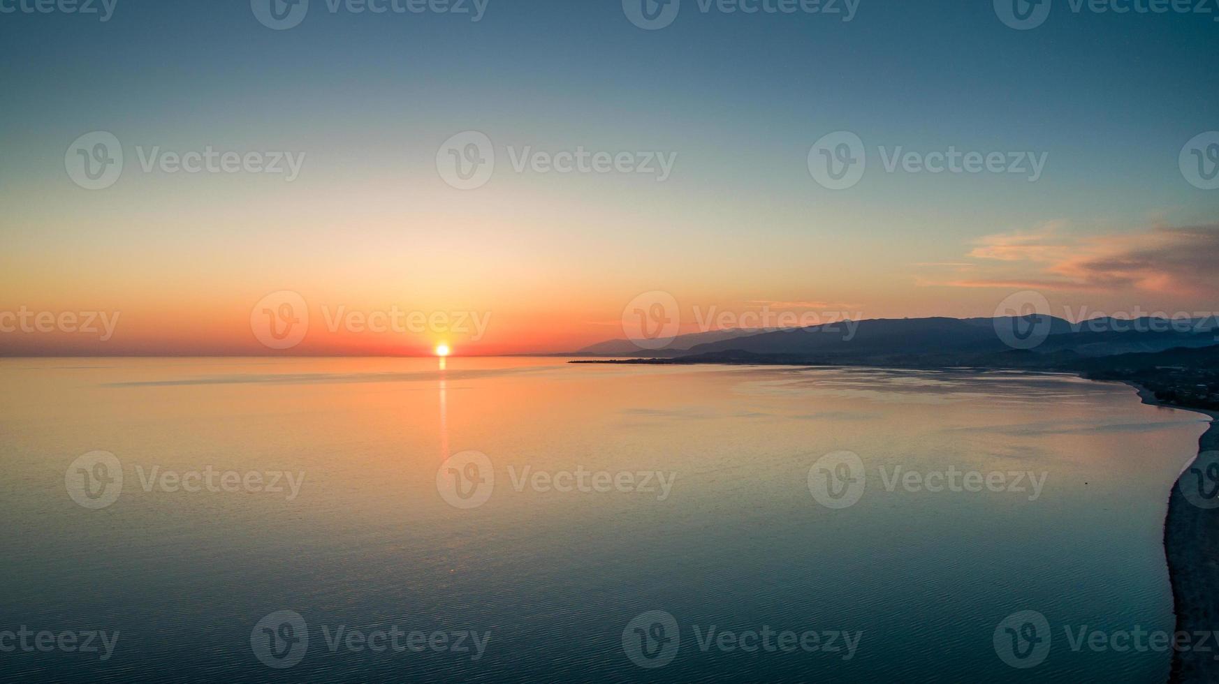 pôr do sol sobre um mar calmo do alto do voo dos pássaros foto