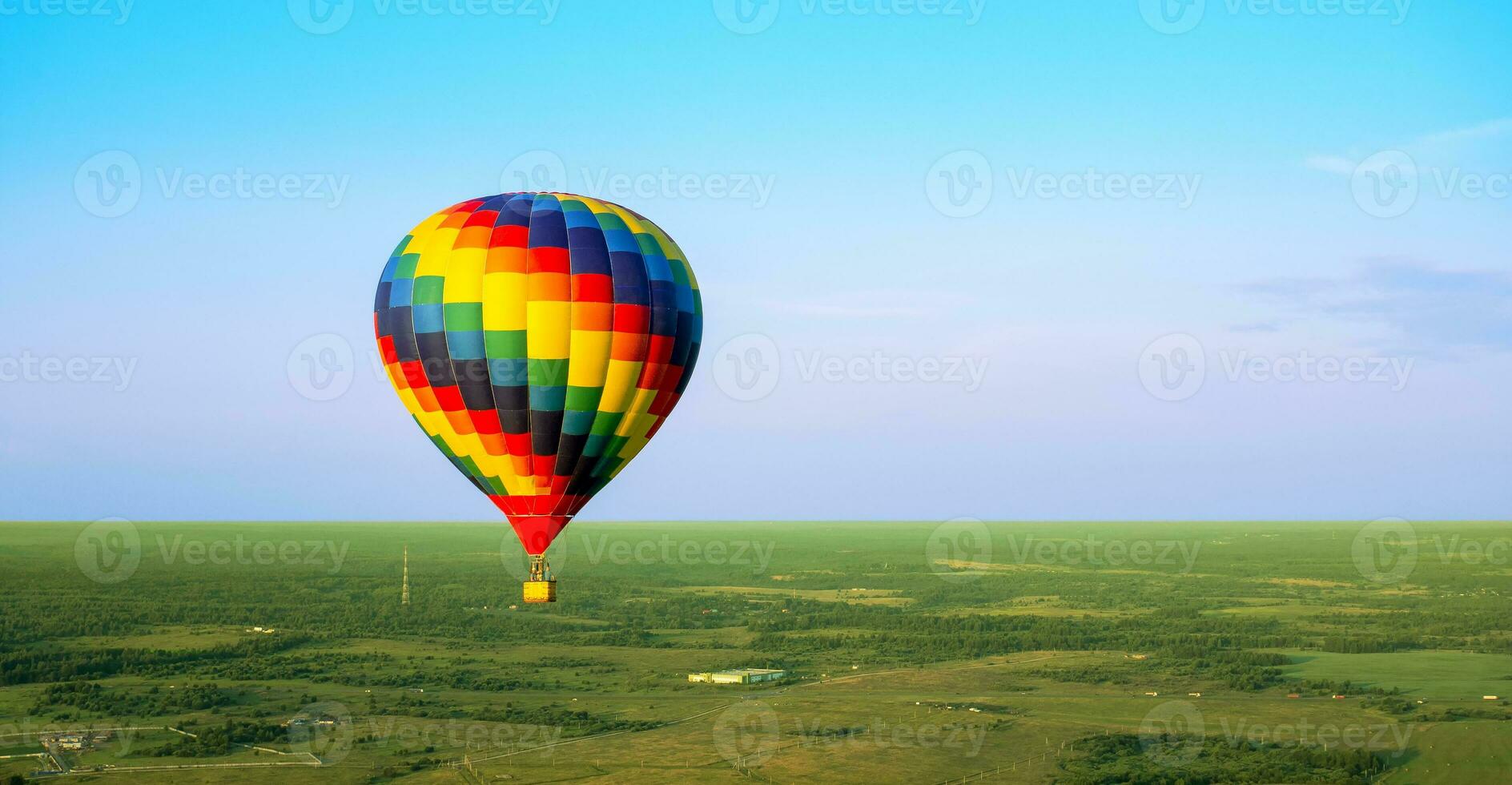 um balão de ar colorido está voando em voo livre sobre o campo. vista aérea. balão multicolorido no céu azul foto