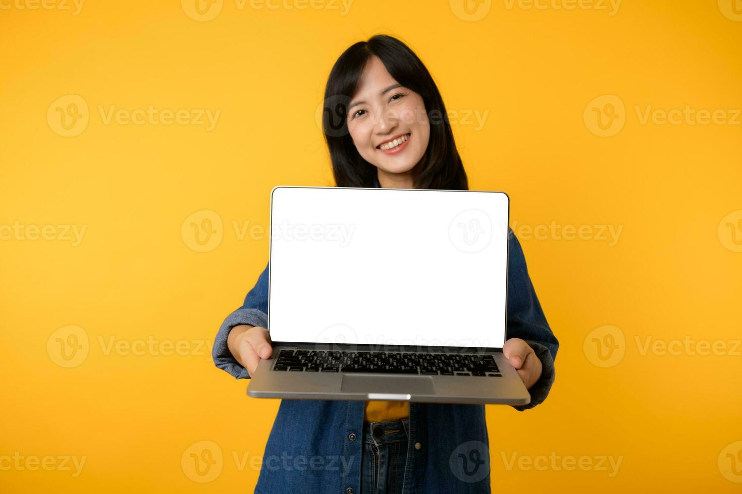 retrato jovem feliz mulher vestindo amarelo camiseta e jeans camisa segurando computador portátil e ponto dedo para tela isolado em amarelo estúdio fundo. o negócio tecnologia inscrição comunicação conceito. foto