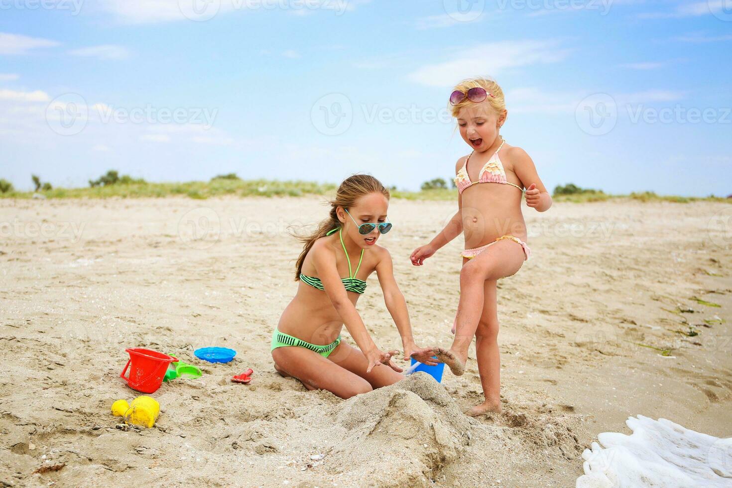 crianças jogar com areia em de praia. menina rompe castelo do areia, namorada gritos. foto