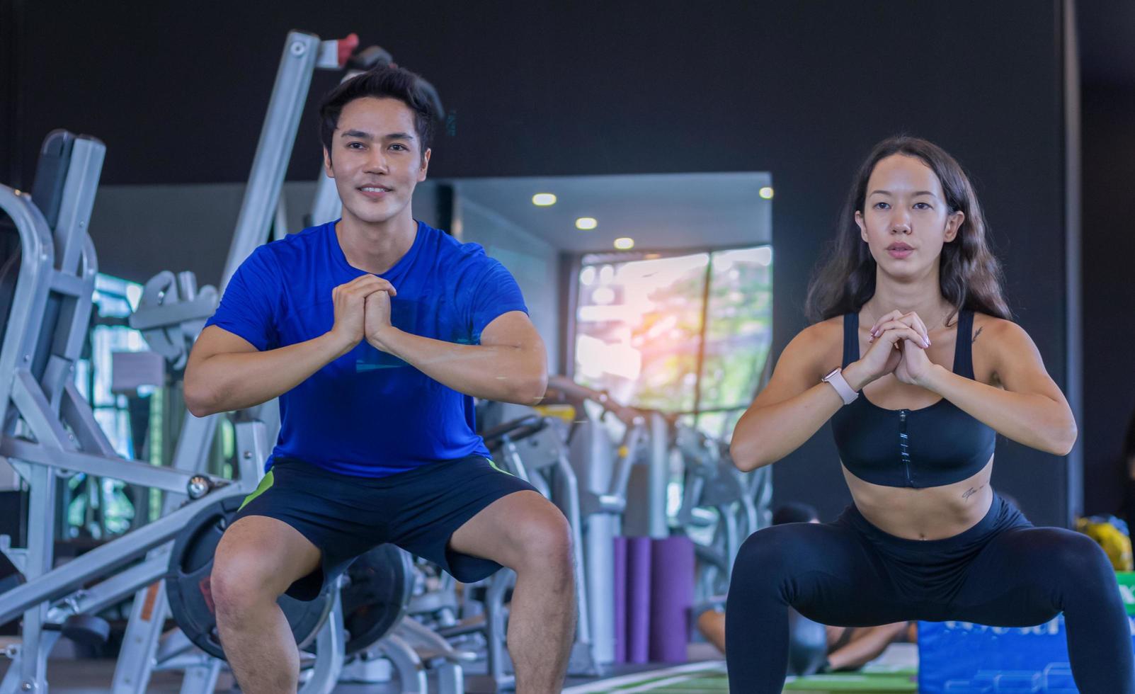 linda mulher asiática se exercitando em uma academia com um personal trainer homem bonito fitness foto