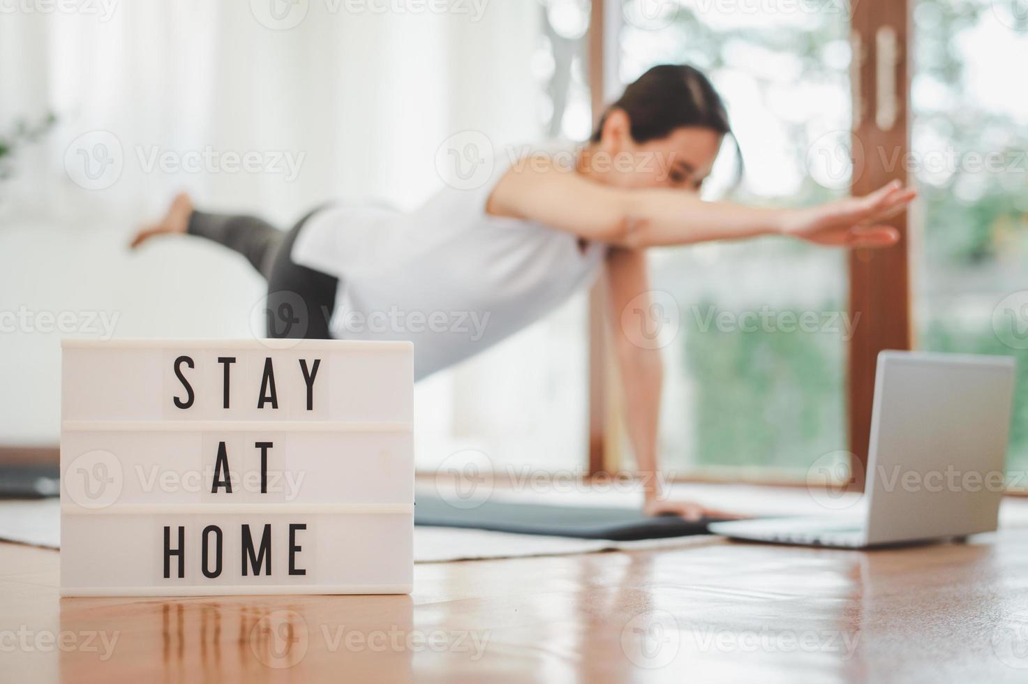 ficar em casa assinar lightbox com mulher praticando ioga alongamento de exercícios via laptop na sala de estar em casa no fundo auto-isolamento e treino em casa foto