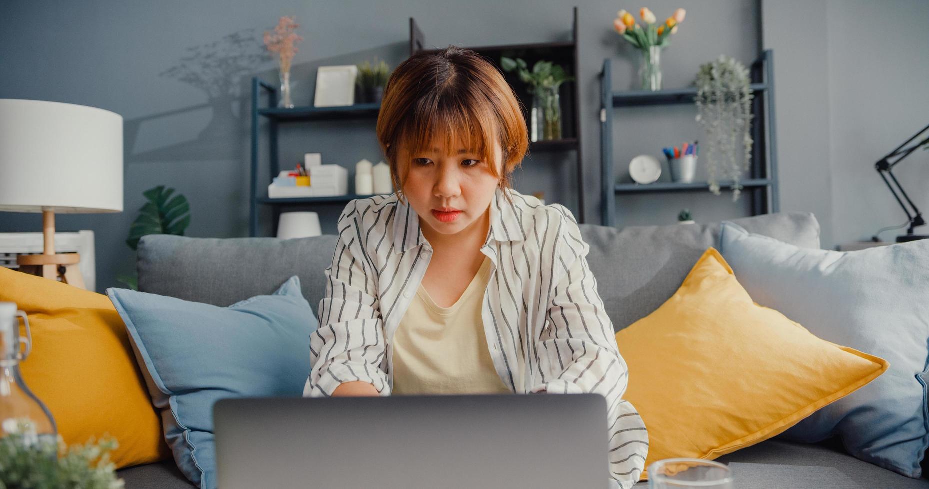 roupa casual para senhora freelance asiática usando laptop aprendizagem on-line na sala de estar foto