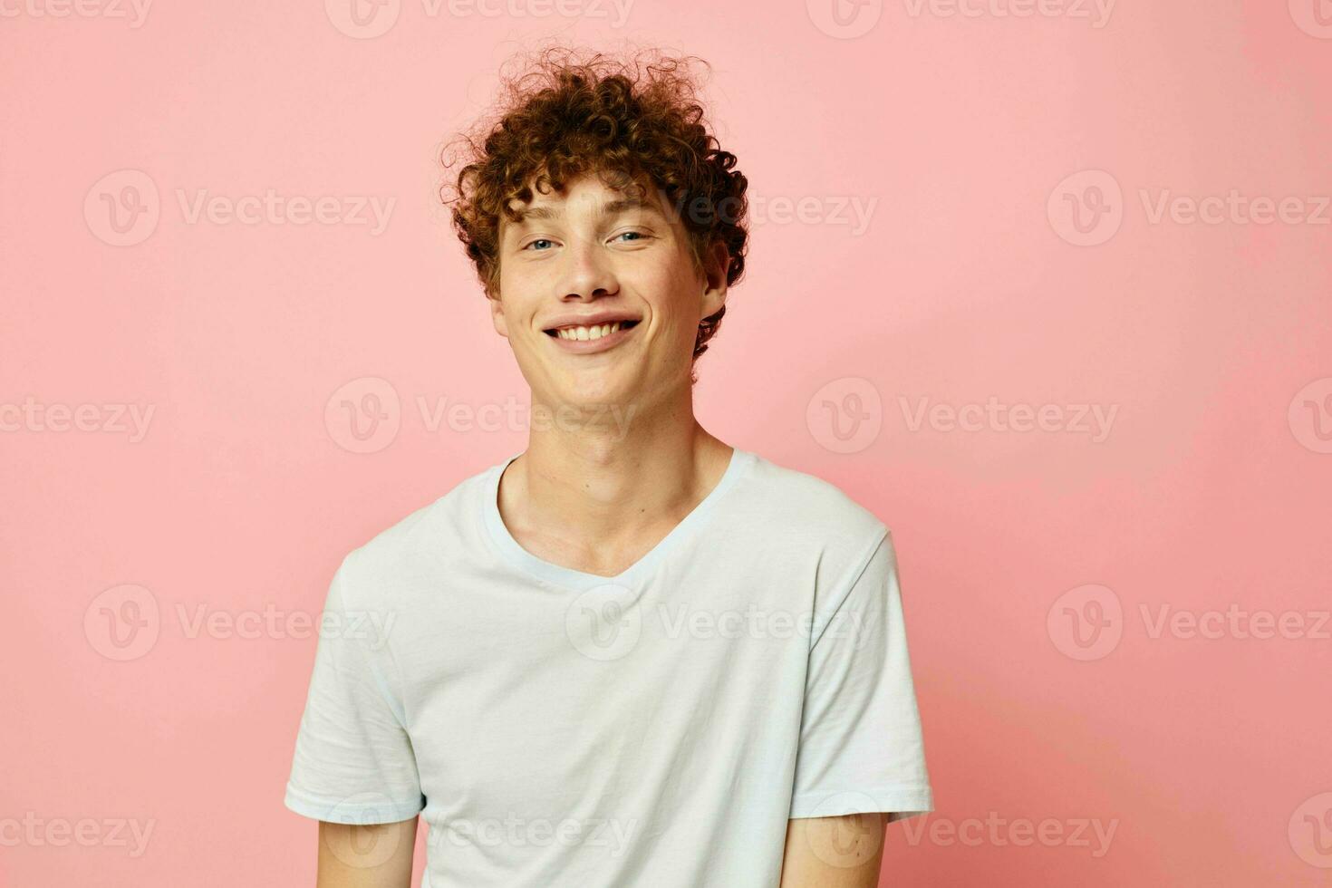 retrato do uma jovem encaracolado homem dentro branco camiseta casual vestem emoções Rosa fundo inalterado foto