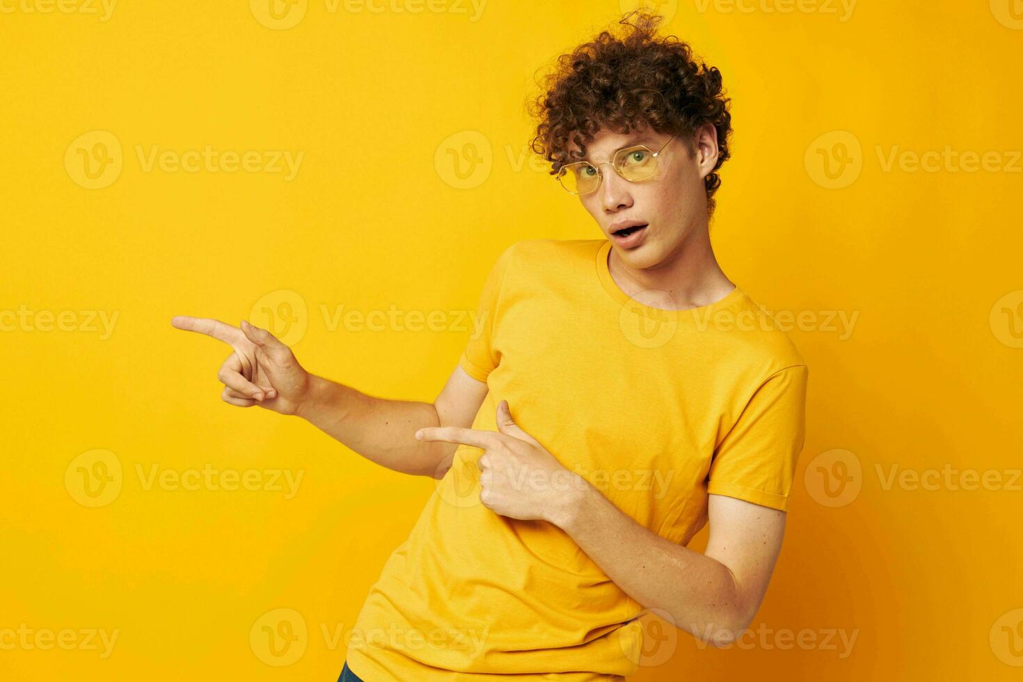retrato do uma jovem encaracolado homem amarelo camiseta óculos moda mão gestos isolado fundo inalterado foto