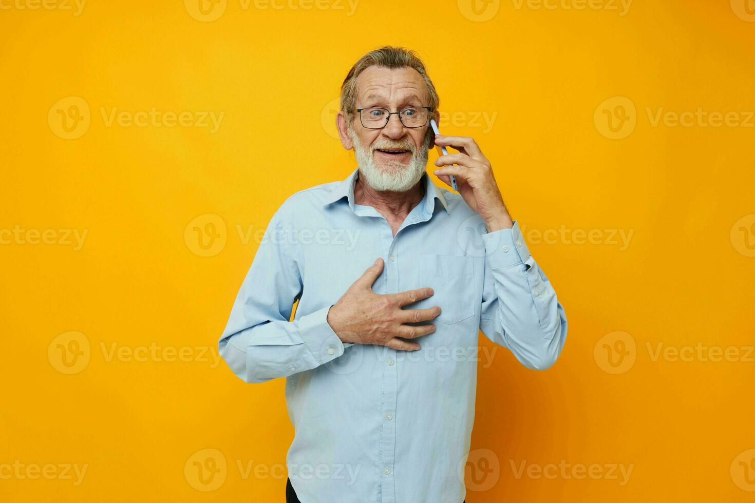 retrato do feliz Senior homem cinzento barba com óculos falando em a telefone amarelo fundo foto