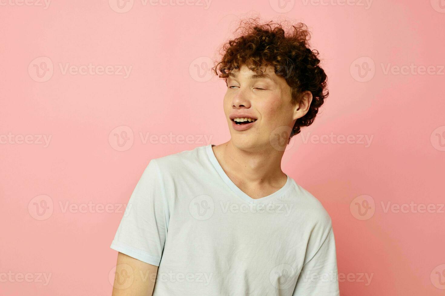 retrato do uma jovem encaracolado homem dentro branco camiseta casual vestem emoções Rosa fundo inalterado foto