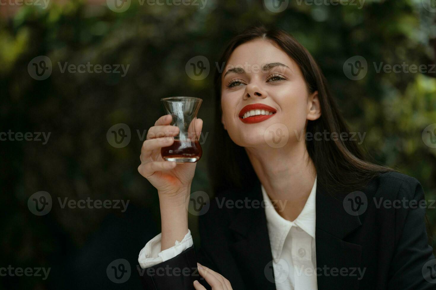 mulher sorrir com dentes bebendo chá dentro uma cafeteria a partir de uma turco vidro caneca em a rua, Primavera viagem, cidade pausa foto