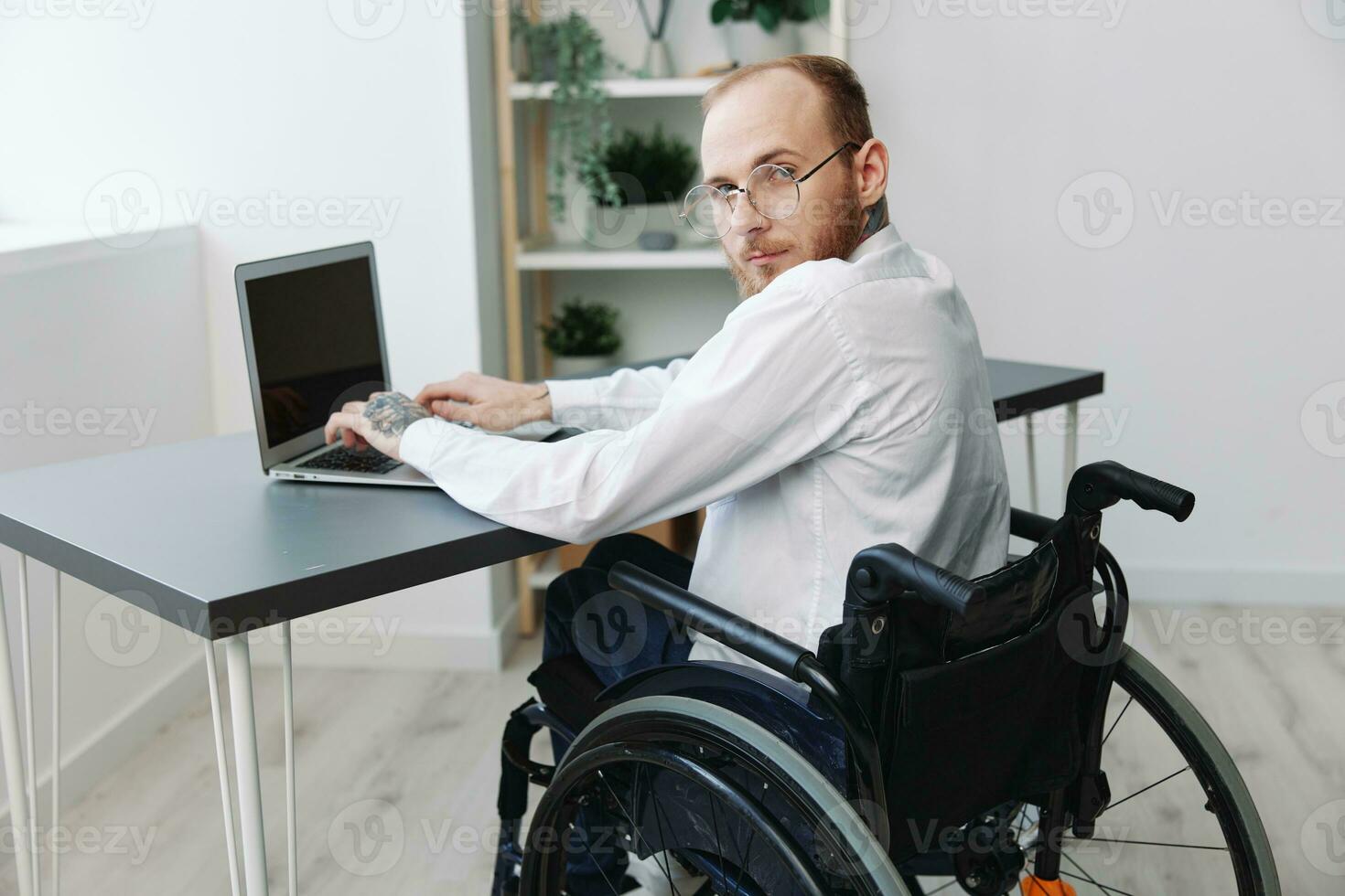 uma homem cadeira de rodas homem de negocios com tatuagens escritório trabalho às uma computador portátil on-line, social redes e comece, integração para dentro sociedade, a conceito do trabalhando uma pessoa com deficiências, Visão a partir de a costas foto