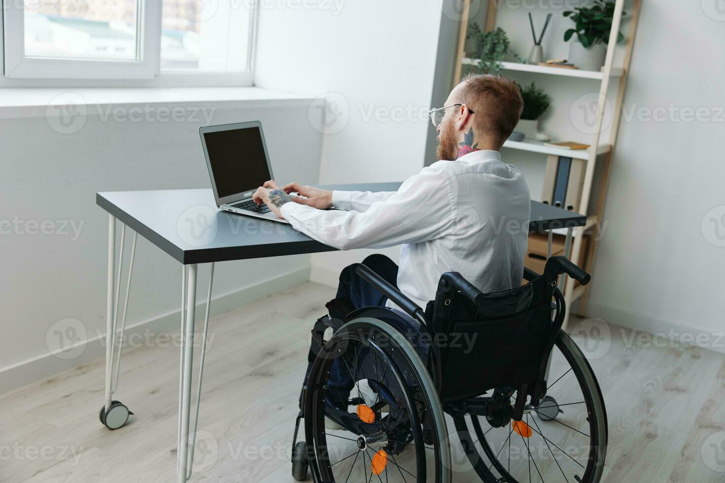 uma homem dentro uma cadeira de rodas parece às a Câmera homem de negocios dentro a escritório trabalhando em uma computador portátil on-line, social redes comece, integração para dentro sociedade, conceito trabalhando pessoa com deficiências, Visão costas foto