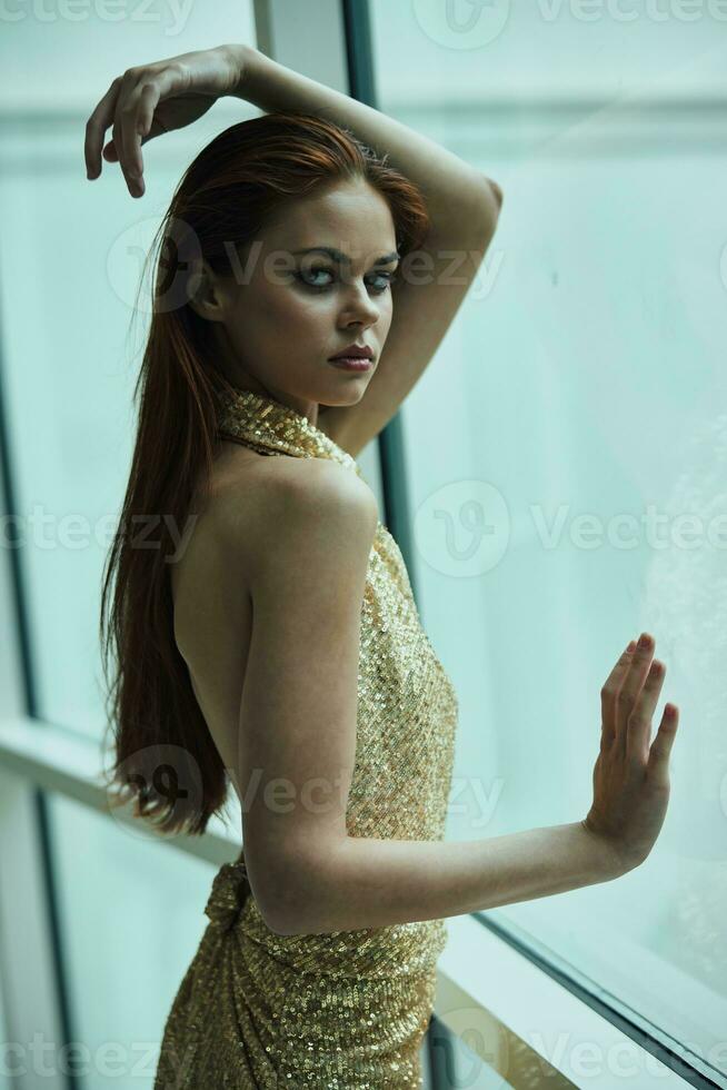 lindo moda mulher dentro à moda caro ouro lantejoulas vestir poses olhando Fora a janela às a cidade dentro uma hotel, Natal festa foto