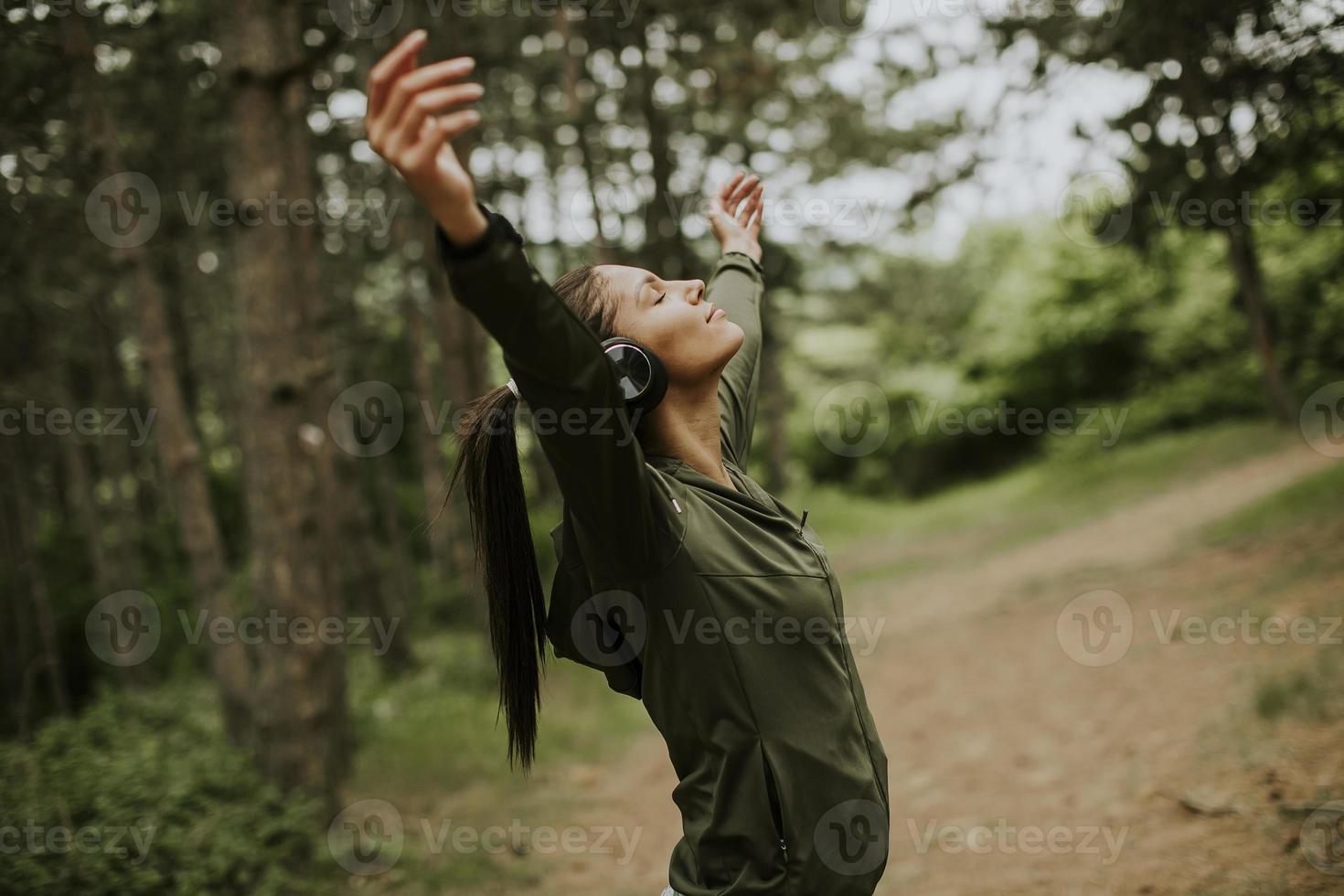 jovem com fones de ouvido espetando os braços na floresta porque gosta de treinar ao ar livre foto