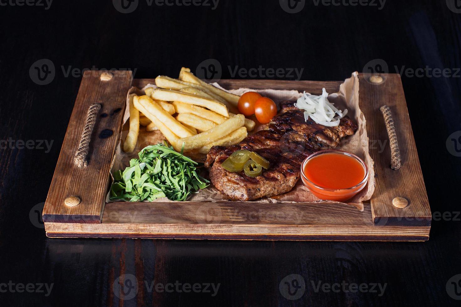 bife de filé com batatas fritas em uma bandeja de madeira, bela porção, fundo escuro foto