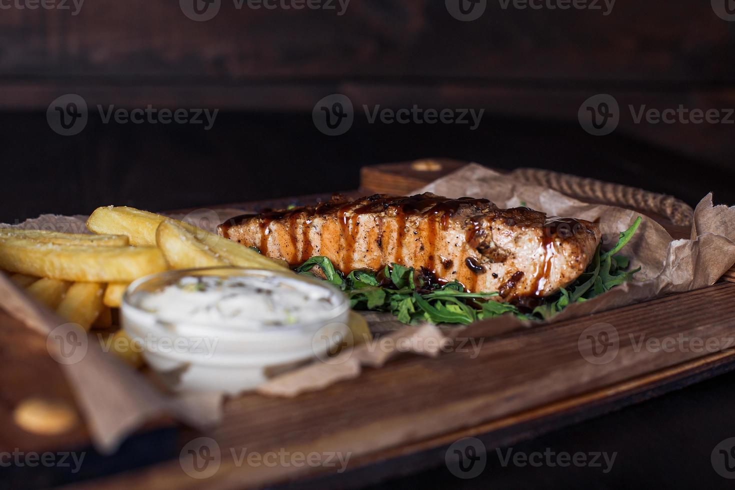 Filé de salmão com batatas fritas em uma bandeja de madeira, bela porção, fundo escuro foto