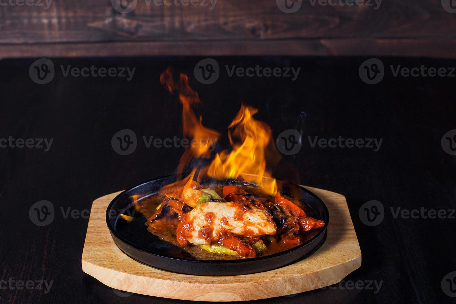 fajitos, carne em uma frigideira com fogo em uma bandeja de madeira, bela porção, fundo escuro foto