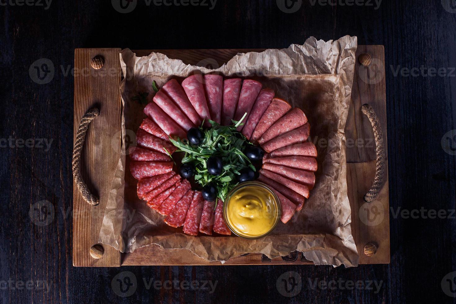 salsicha cortada com ervas e molho em uma bandeja de madeira, bela porção, fundo escuro foto