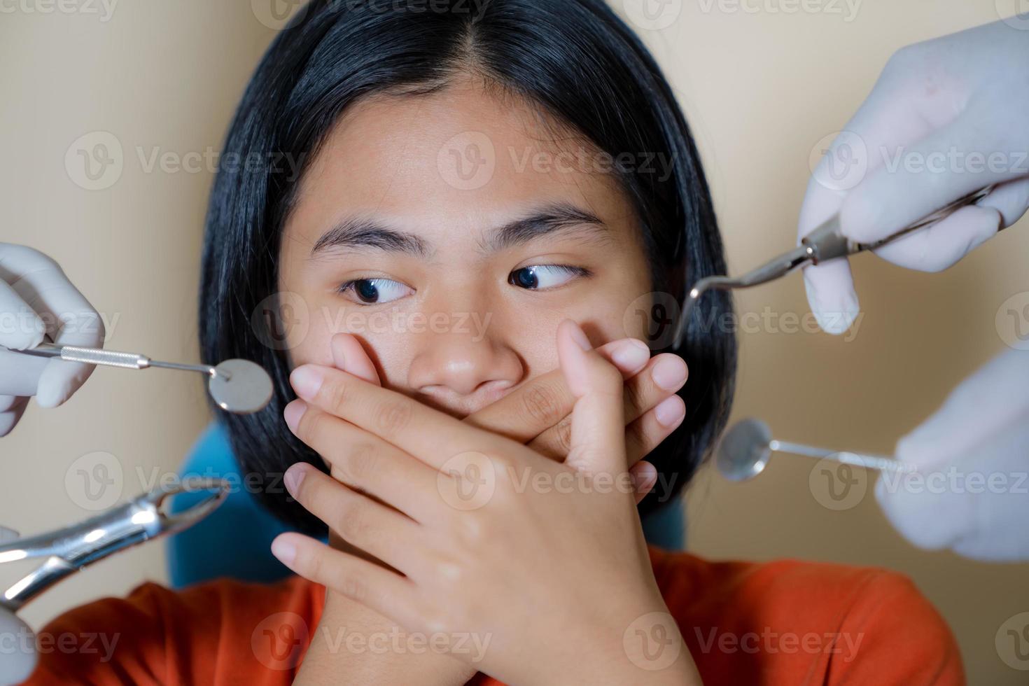 menina assustada com dentistas cobre a boca no consultório do dentista foto