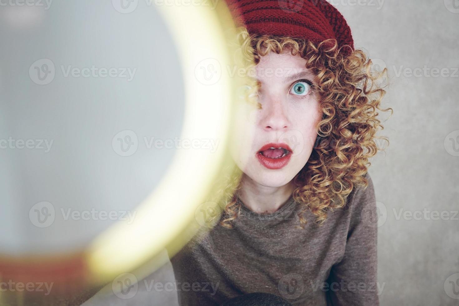 closeup retrato de uma bela e jovem mulher engraçada com olhos azuis e cabelo loiro encaracolado investigando com uma lupa e ela fica surpresa foto