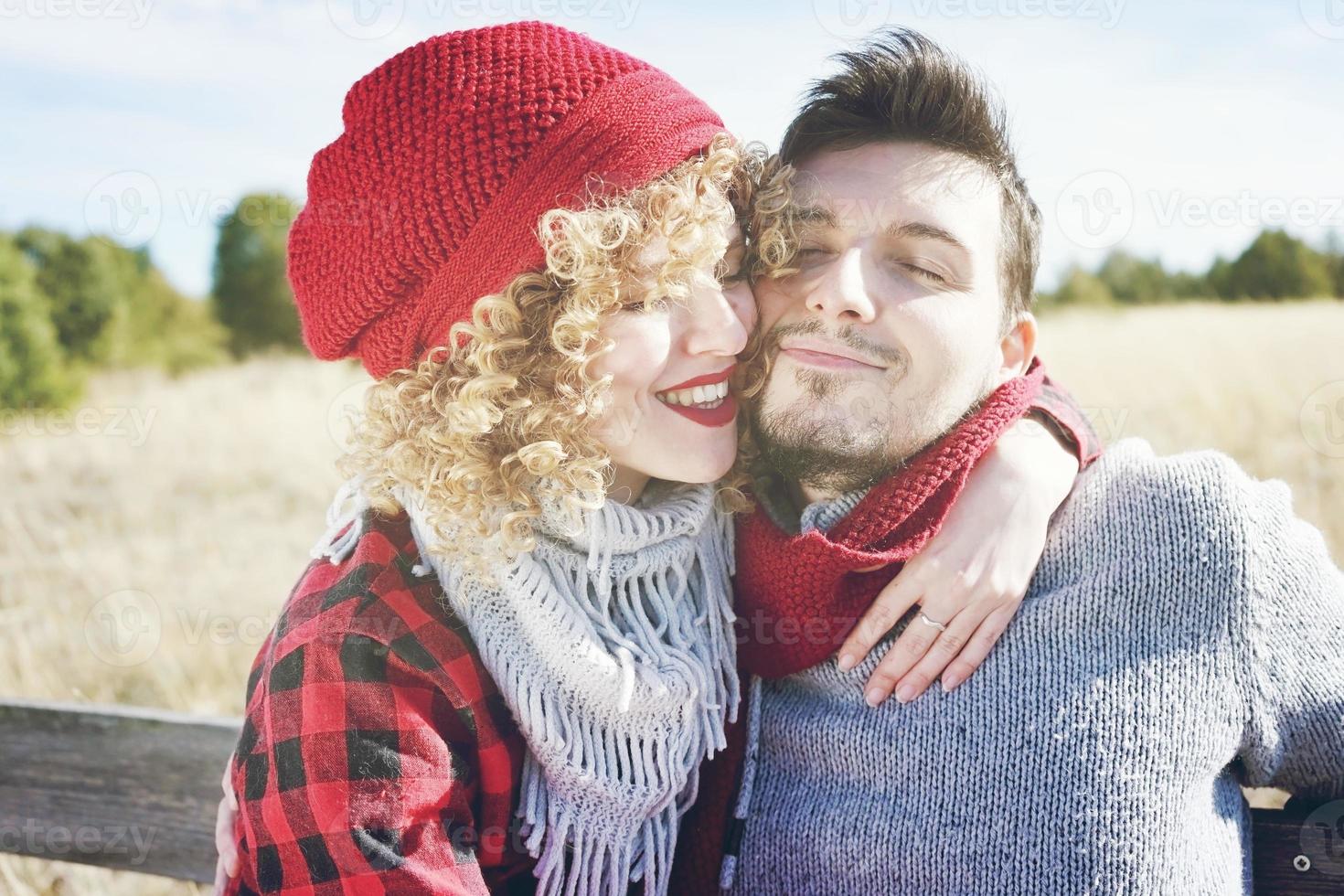 jovem casal romântico de uma linda mulher loira com cabelo encaracolado e usando um boné de lã vermelha, abraços para o namorado e um homem bonito ao ar livre foto