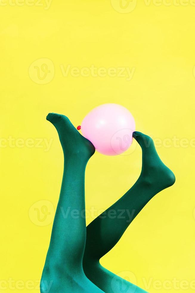 pernas verdes de uma mulher segurando um balão rosa contra uma parede amarela foto
