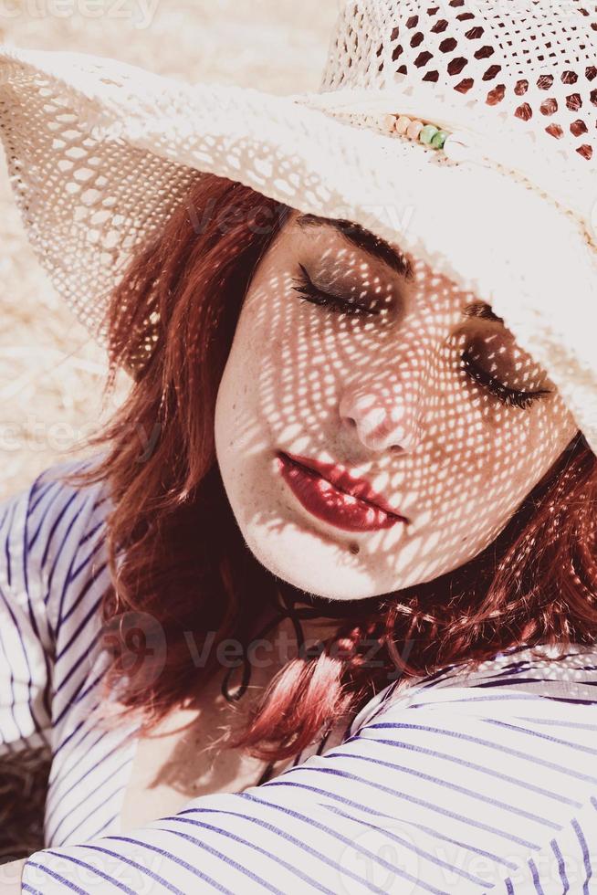 modelo ruiva se protegendo do sol com um chapéu no verão foto