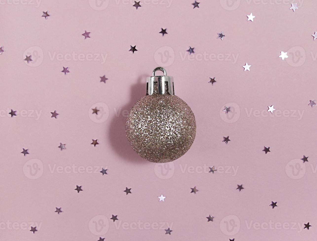 glitter bola de árvore de Natal e estrelas de confetes em um papel rosa. lay plana festiva. foto