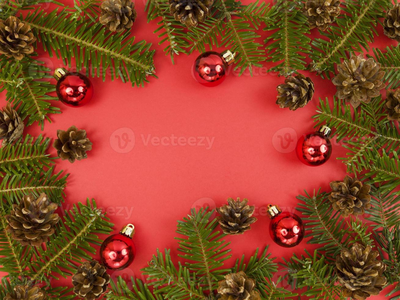 cartão postal de férias com galhos de árvore do abeto, cones e enfeites vermelhos sobre um fundo vermelho. Natal plana deitar-se com espaço de cópia. foto