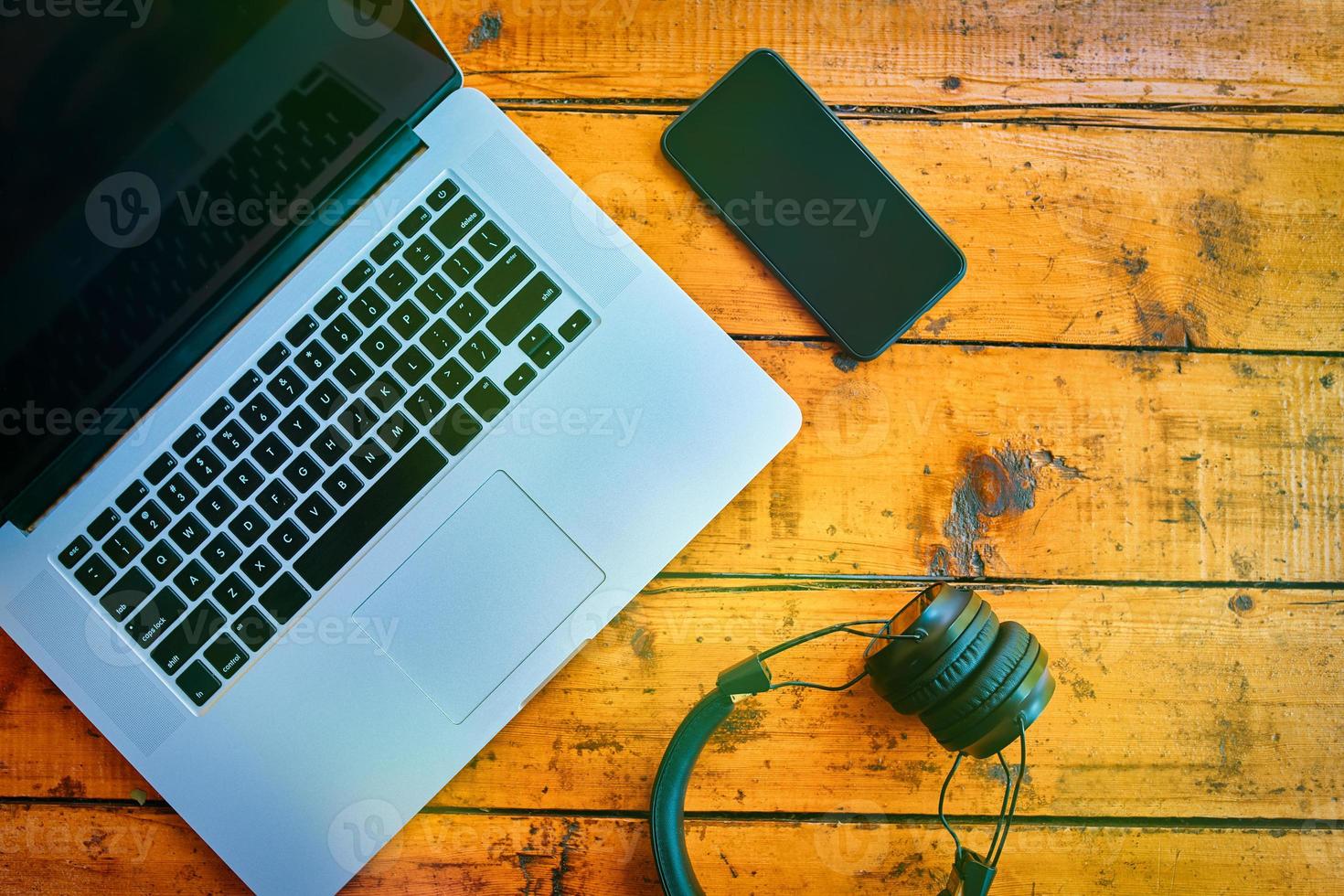 postura plana do laptop, fones de ouvido sem fio e telefone celular na mesa de madeira. foto