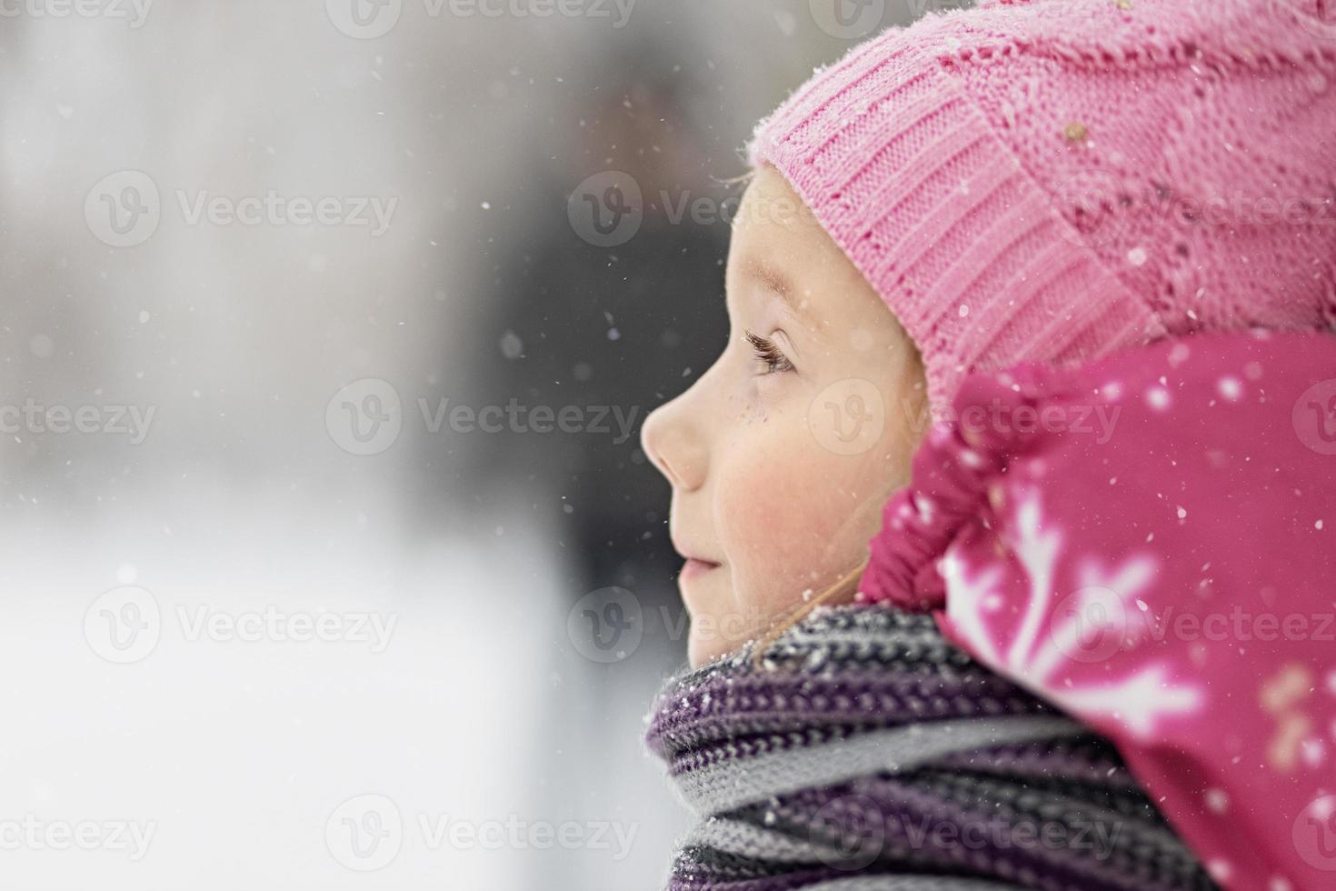 retrato de uma menina em close-up rosa. uma criança gosta da queda de neve. feriado de Natal foto