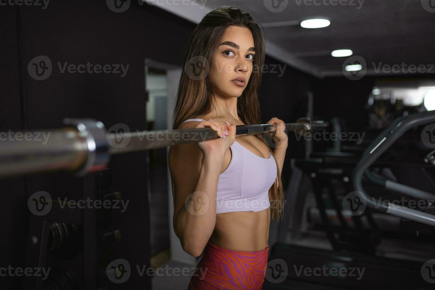 sexy Atlético esporte menina com perfeito ginástica corpo fazendo exercite-se Difícil Treinamento com Barra dentro a Academia foto